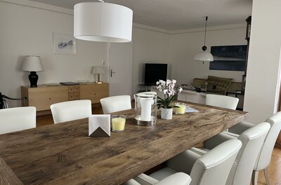 Rustikaler Holztisch mit weißen Lederstühlen in einem hellen Esszimmer.