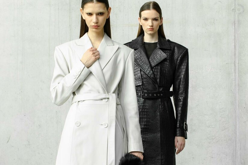 Zwei Models in langen Mänteln vor einer Betonwand.