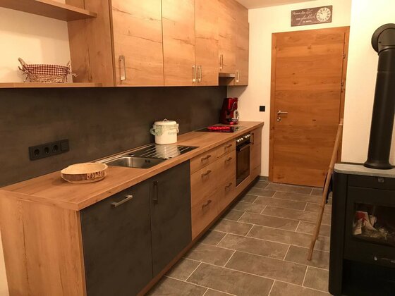 Moderne Küchenzeile aus Holz und dunklem Stein mit Herd, Spüle und angrenzendem Kaminofen.