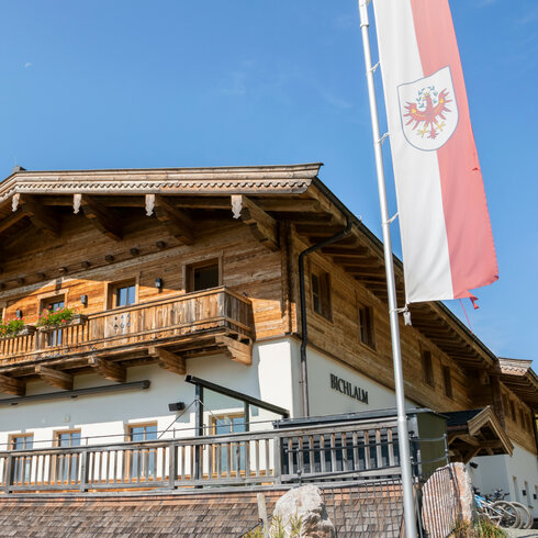 Ein traditionelles Holzhaus mit einem Balkon, geschmückt mit bunten Blumen, unter einem strahlend blauen Himmel.