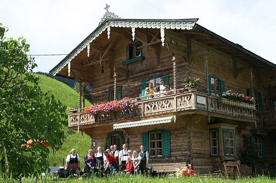 Sommer Familie beim Kainzergütl Traditionelles Holzhaus mit einer Gruppe von Menschen in Tracht davor und auf dem Balkon.