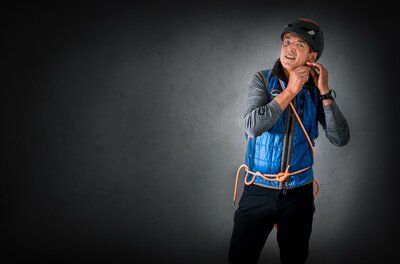 Ein Sportler bereitet sich auf das Klettern vor und trägt einen Helm. Er hat eine Kletterausrüstung und schaut fokussiert in die Kamera.