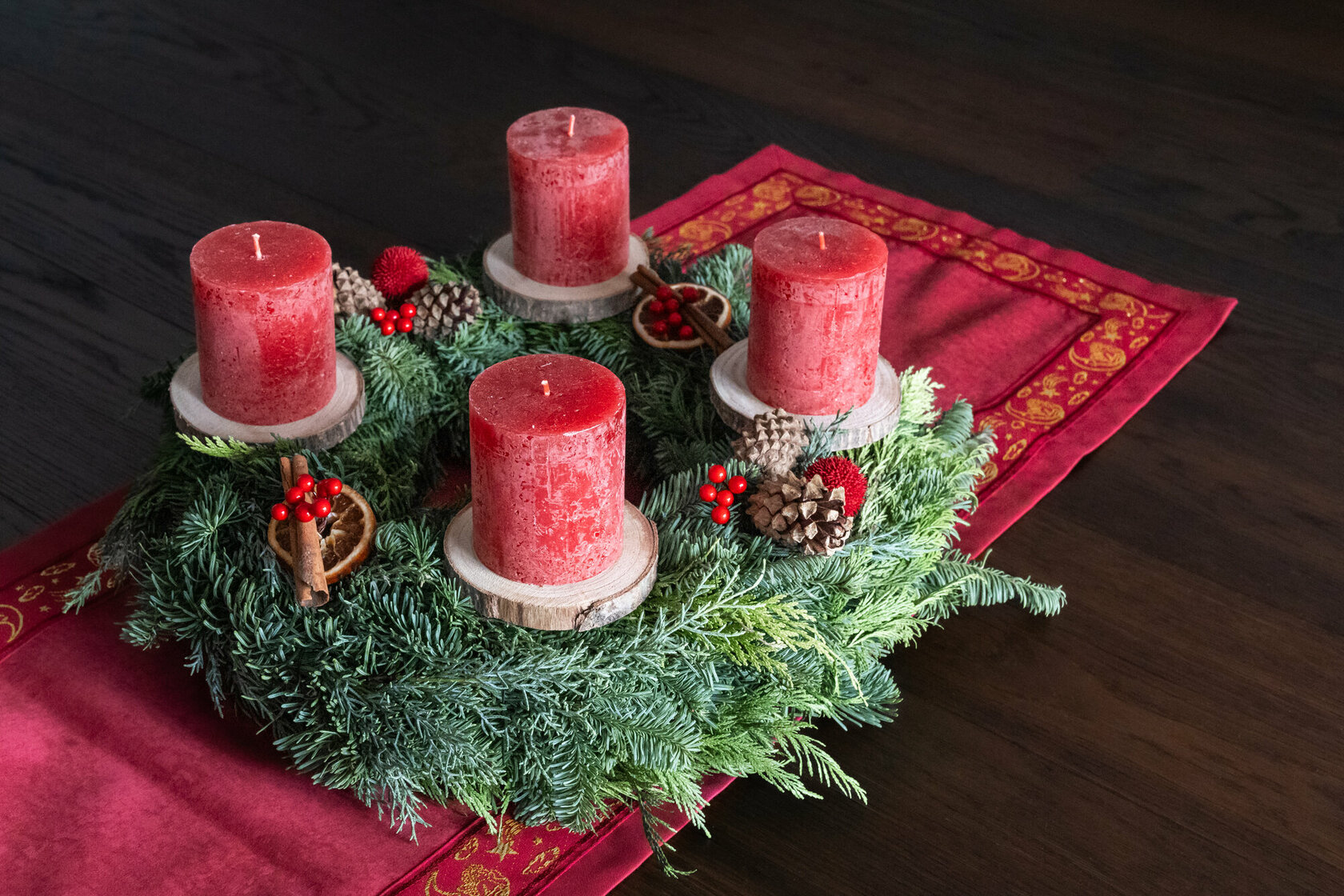 A green Advent wreath with four red candles on a red tablecloth.