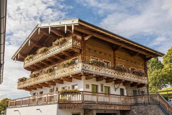 Aussenansicht Rosi´s Sonnbergstuben Chalet Mehrstöckiges Holzchalet mit blumengeschmückten Balkonen vor blauem Himmel.
