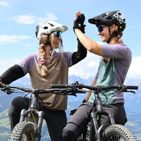 In Kitzbühel geben sich zwei Mountainbikerinnen auf einer Wiese ein High-Five und feiern ihren Erfolg.