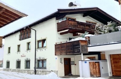 Zweistöckiges weißes Alpenhaus mit Holzbalkonen und schneebedecktem Dach im Winter.