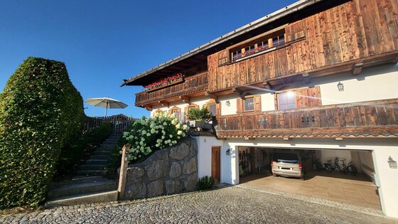 Alpines Holzhaus mit Balkon, Steintreppe und Garage unter blauem Himmel.