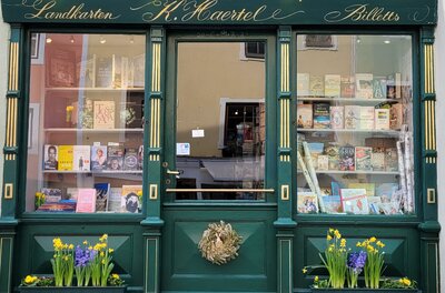 Grüne Fassade der Buchhandlung Bücherklause mit Schaufenstern, goldener Schrift und Blumenkästen.