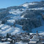 Eine verschneite Berglandschaft mit einem kleinen Dorf im Vordergrund und einer Kirche, umgeben von schneebedeckten Bäumen.