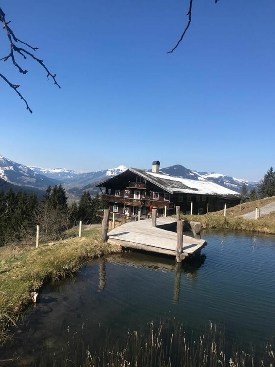 Holzhütte mit Steg an einem kleinen Teich vor schneebedeckten Bergen.