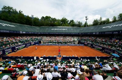 Blick von der Tribüne auf einen Sand-Tennisplatz während eines Turniers mit vielen Zuschauern.