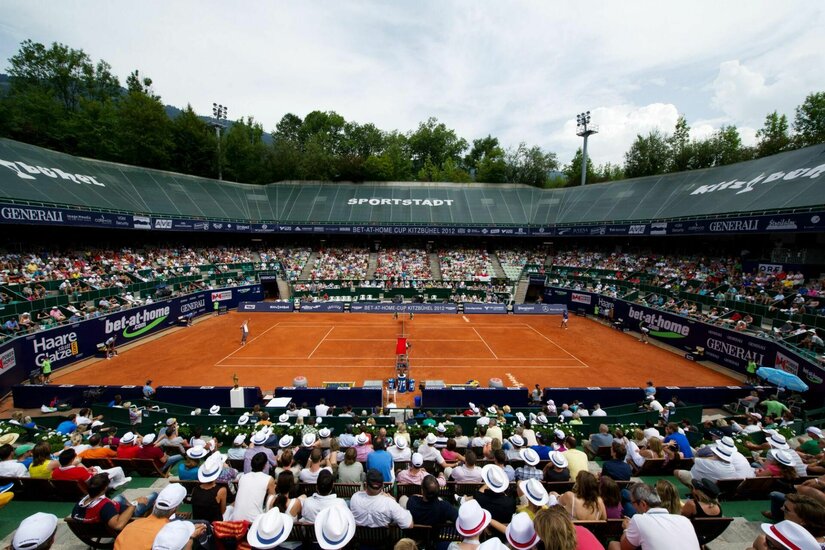 Blick von der Tribüne auf einen Sand-Tennisplatz während eines Turniers mit vielen Zuschauern.
