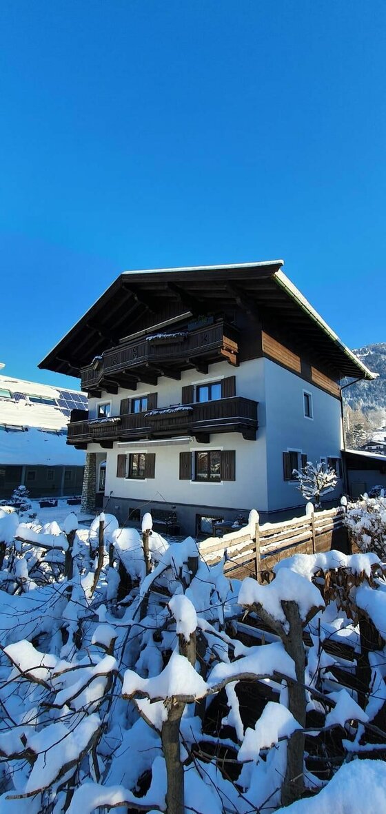 Haus Pankratz im Winter Mehrstöckiges alpines Wohnhaus mit Holzbalkonen im Winter vor blauem Himmel.