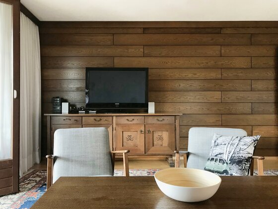 Wohnzimmer Hahnenkamm Wohnzimmer mit Holzvertäfelung, Fernseher auf Sideboard und zwei Sesseln vor einem Tisch.