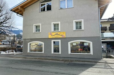 Lanna Thai Imbiss Ein modernes Gebäude mit grau gestrichener Fassade und großen Fenstern. An der Wand ist ein leuchtendes Schild angebracht, das Aufmerksamkeit erregt.