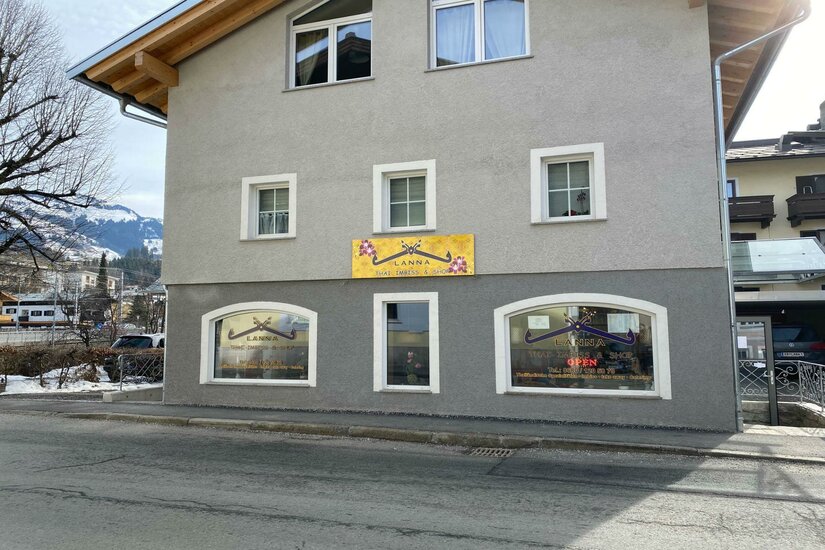 Ein modernes Gebäude mit grau gestrichener Fassade und großen Fenstern. An der Wand ist ein leuchtendes Schild angebracht, das Aufmerksamkeit erregt.
