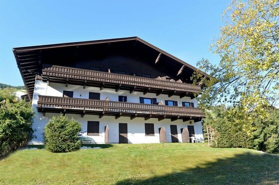Mehrstöckiges weißes Gebäude mit dunklen Holzbalkonen und flachem Satteldach vor blauem Himmel.