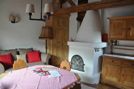 Rustikaler Wohnraum mit weißem Kachelofen, Holztisch und Sofa.