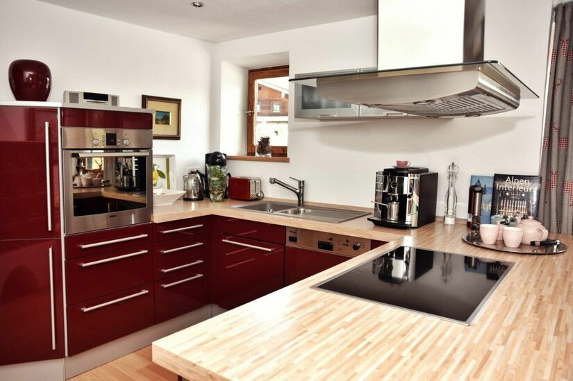 Jagahäusl Küche Moderne Einbauküche mit weinroten Fronten, Holz-Arbeitsplatte, Induktionskochfeld und Kaffeemaschine.