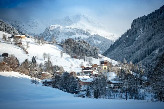 Ortsansicht Aurach im Winter Verschneites Bergdorf mit Kirchturm vor bewaldeten Hängen und schneebedeckten Gipfeln.