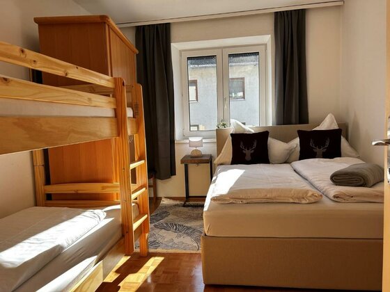 Ein gemütliches Schlafzimmer mit einem Doppelbett und einem Etagenbett. Große Fenster sorgen für viel Tageslicht.