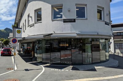 Ein mehrstöckiges Gebäude mit einer großen Glasfront im Erdgeschoss und einer Bushaltestelle davor.
