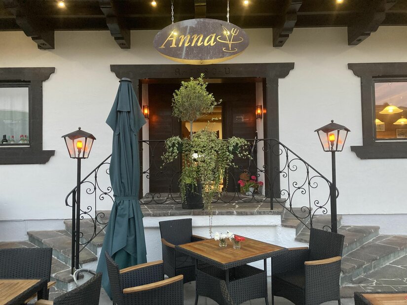 Restaurant Anna Außenansicht Eingangsbereich des Restaurants Anna mit Außenterrasse, Holztischen, schwarzen Stühlen und beleuchteten Laternen.
