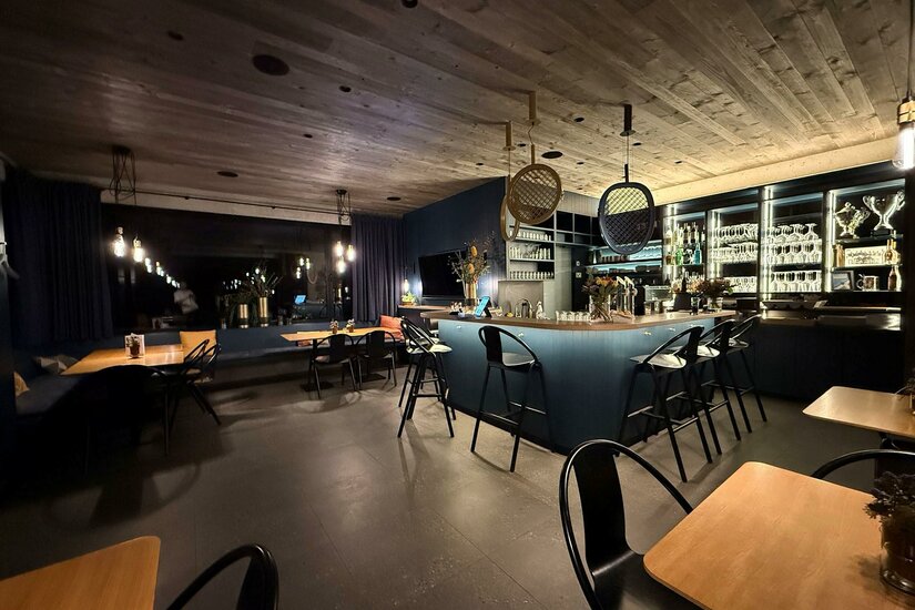 Eine moderne Bar mit gemütlichen Tischen und Stühlen. Das Beleuchtungskonzept schafft eine einladende Atmosphäre.