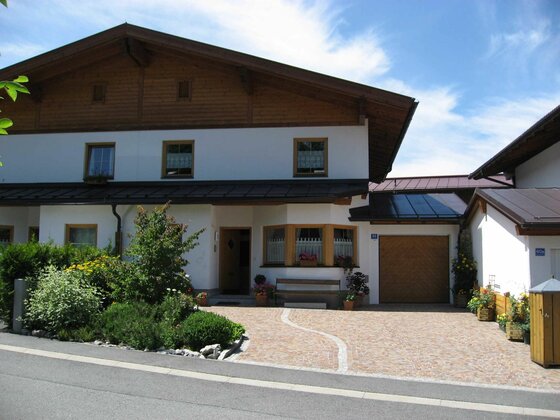 Eingangsbereich Haus Aschenwald Vorderansicht eines zweistöckigen Wohnhauses mit weißer Fassade, Holzgiebel und gepflasterter Einfahrt.