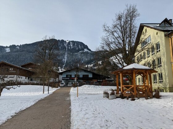 Ortsansicht mit Einsiedelei Verschneiter Weg im Ort mit Holzpavillon, Gebäuden und bewaldetem Berg im Hintergrund.