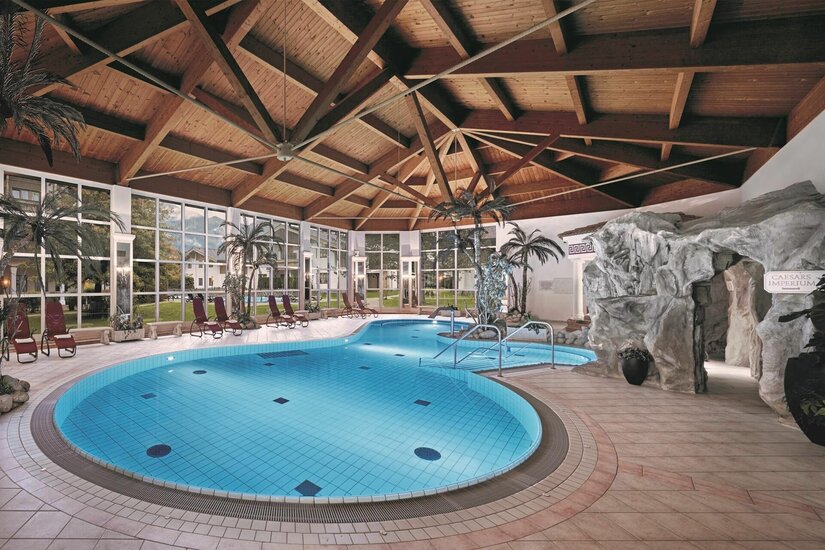 Wellnessbereich Lisi Family Hotel Hallenbad mit Holzdecke, Palmen, Liegestühlen und einer künstlichen Felsengrotte.