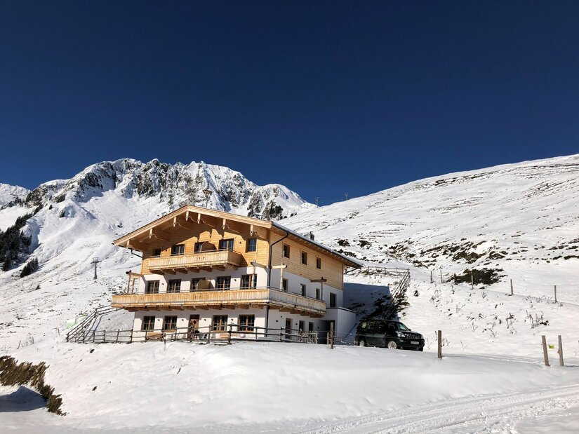 TrattenbachSuits im Winter Mehrstöckiges Holzchalet in einer verschneiten Gebirgslandschaft unter blauem Himmel.