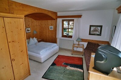 Schlafzimmer mit Doppelbett, Holzverkleidung, Kleiderschrank, Sofa und Fernseher.