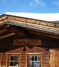 Holzfassade der Jagerwurzhütte mit Namensschild und schneebedecktem Dach unter blauem Himmel.