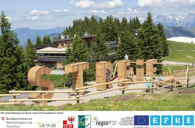 Große Holzbuchstaben als Spielgeräte vor einer Almhütte in den Bergen.