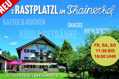 Außenansicht des Thainerhofs mit Terrasse, Sonnenschirmen und umliegenden Bäumen unter blauem Himmel.