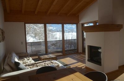 Moderner Wohnraum mit Sofa, Kamin und großem Panoramafenster mit Blick auf eine verschneite Winterlandschaft.