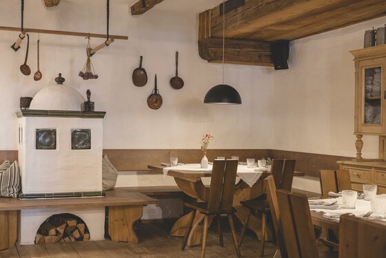 Rustikale Gaststube mit Kachelofen, Holztischen und traditioneller Wanddekoration.