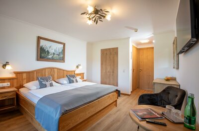 Hotel_Zimmermann_Griesbachweg_48_Reith_bei_Kitzbue Ein modernes Schlafzimmer mit einem großen Doppelbett und Holz-Möbeln. Es gibt einen gemütlichen Sessel und eine große Fensterfront, die für viel Licht sorgt.
