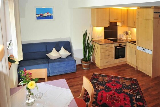 Wohnküche Appartement 31 Wohnküche mit blauem Sofa, Holzküche und Esstisch.