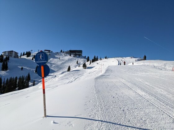 Winterwanderweg bei St. Bernhard Präparierter Winterwanderweg in einer verschneiten Berglandschaft mit blauem Hinweisschild im Vordergrund.