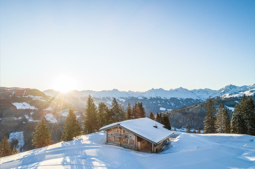 Holzhütte in verschneiter Berglandschaft bei Sonnenaufgang.