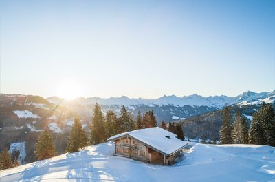 Holzhütte in verschneiter Berglandschaft bei Sonnenaufgang.