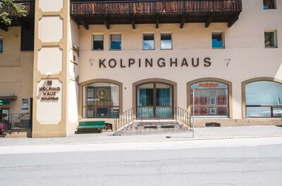 Ein Gebäude mit der Aufschrift "Kolpinghaus" an der Fassade. Es befindet sich in einer ruhigen Umgebung mit Fenster und Eingangstreppe.