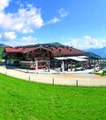 Ein gemütliches Berghaus umgeben von grünen Wiesen und Bergen. Der Himmel ist klar mit einigen Wolken.