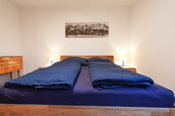 immbolie -1 Ein gemütliches Schlafzimmer mit einem großen Doppelbett und blauen Decken. An den Wänden hängen Bilder, und das Licht ist sanft.