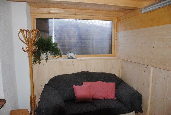 Dunkles Sofa mit rosa Kissen vor einer holzverkleideten Wand und einem Fenster.