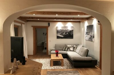 Modernes Wohnzimmer mit Ecksofa, Holztisch und Deckenbalken unter einem Rundbogen.