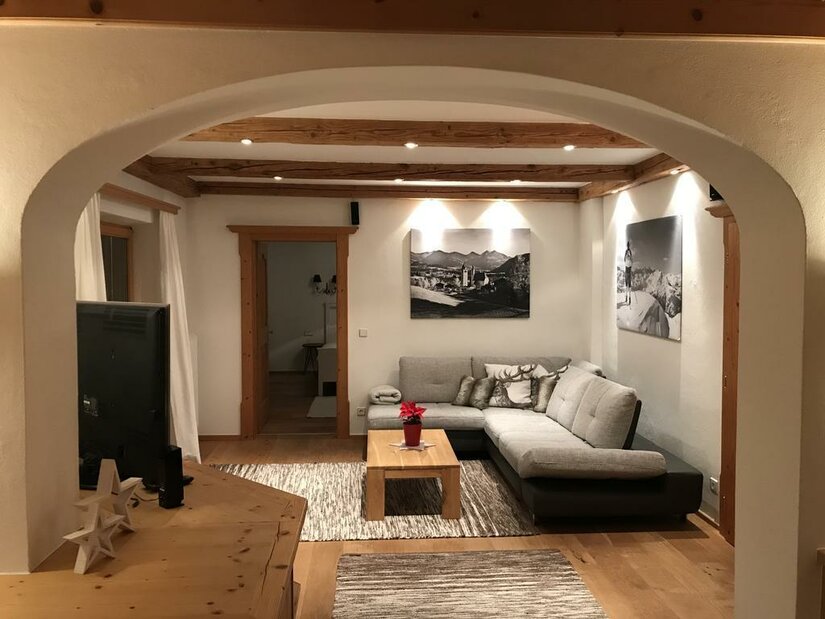 Modernes Wohnzimmer mit Ecksofa, Holztisch und Deckenbalken unter einem Rundbogen.
