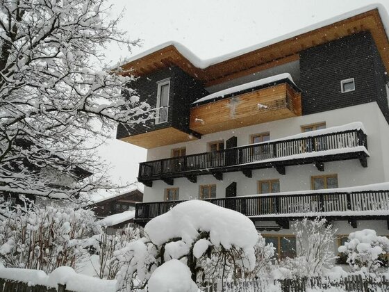 Mehrstöckiges Gästehaus mit Holzbalkonen und schneebedecktem Dach bei Schneefall.